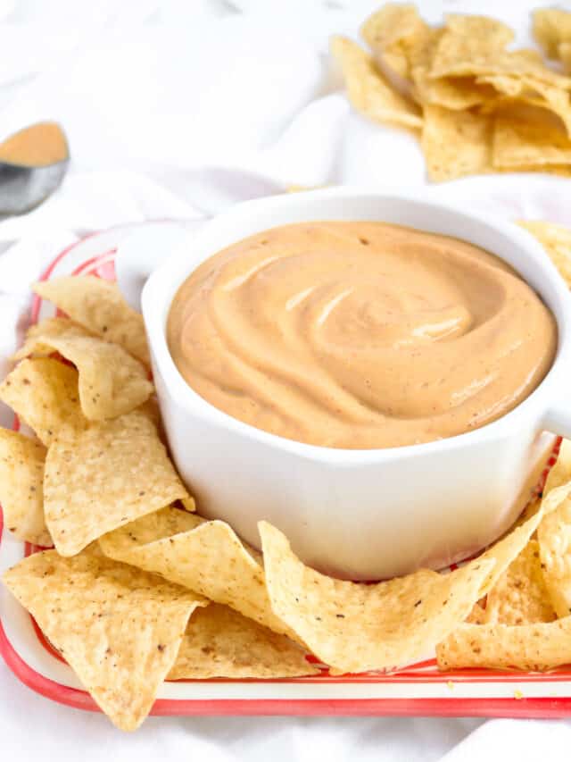 Small bowl of queso surrounded by tortilla chips.