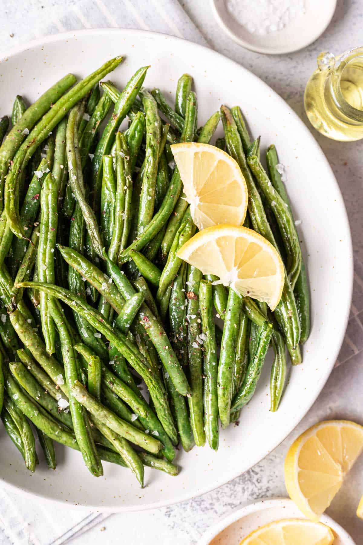 A plate of air fryer green beans garnished with fresh lemon wedges.