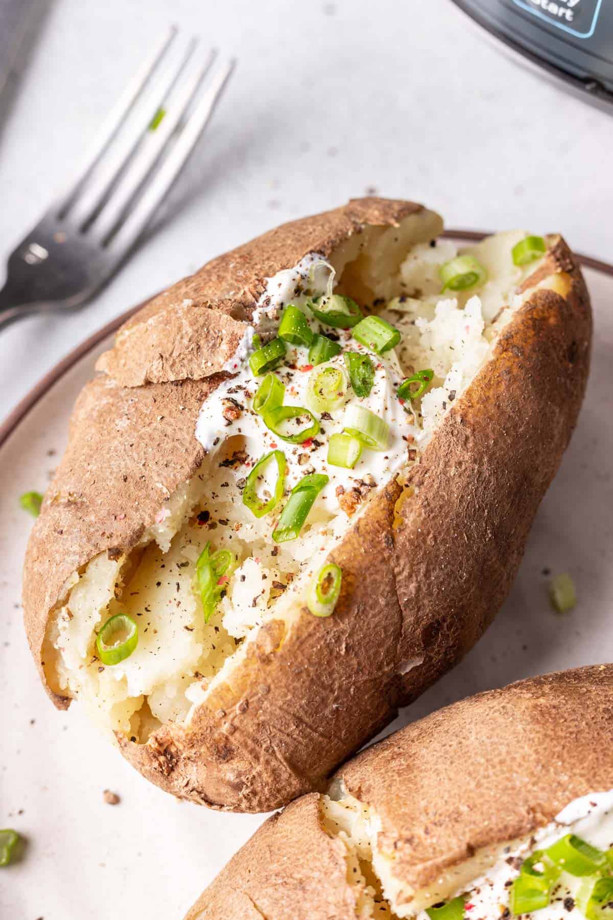 Baked potato loaded with sour cream, green onion, and seasonings on plate.