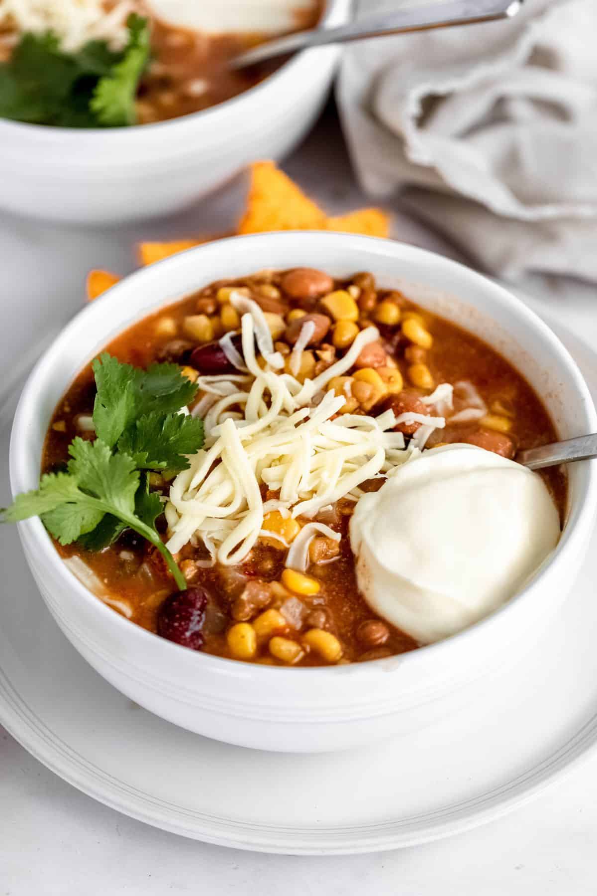 Two bowls of taco soup garnished with cheese, sour cream and cilantro.