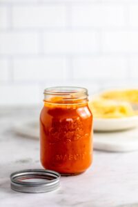 Spaghetti sauce in jar with pasta in background.