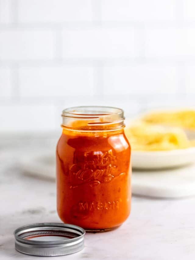 Spaghetti sauce in jar with pasta in background.