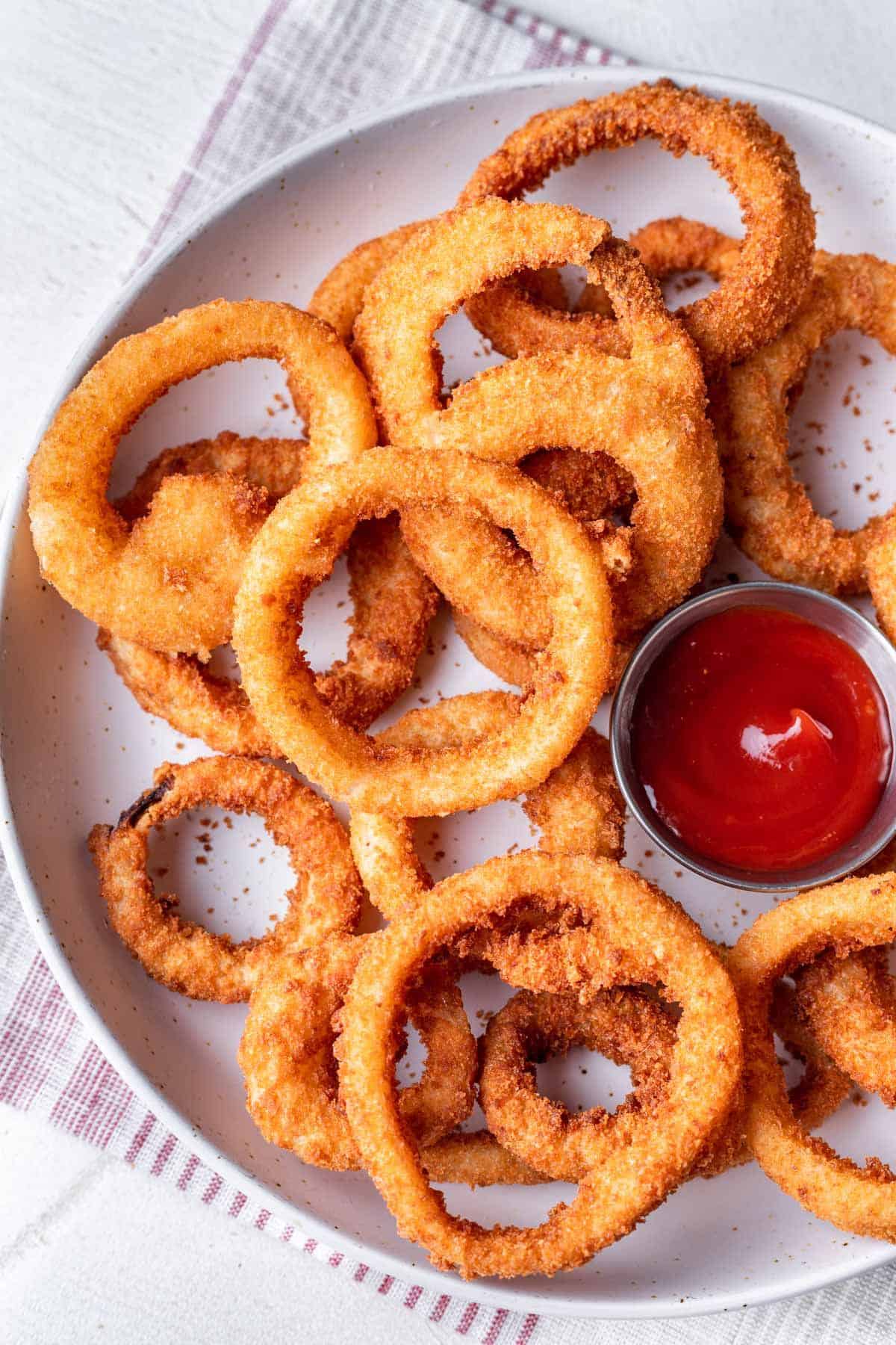 Onion rings on serving plate with side of ketchup..