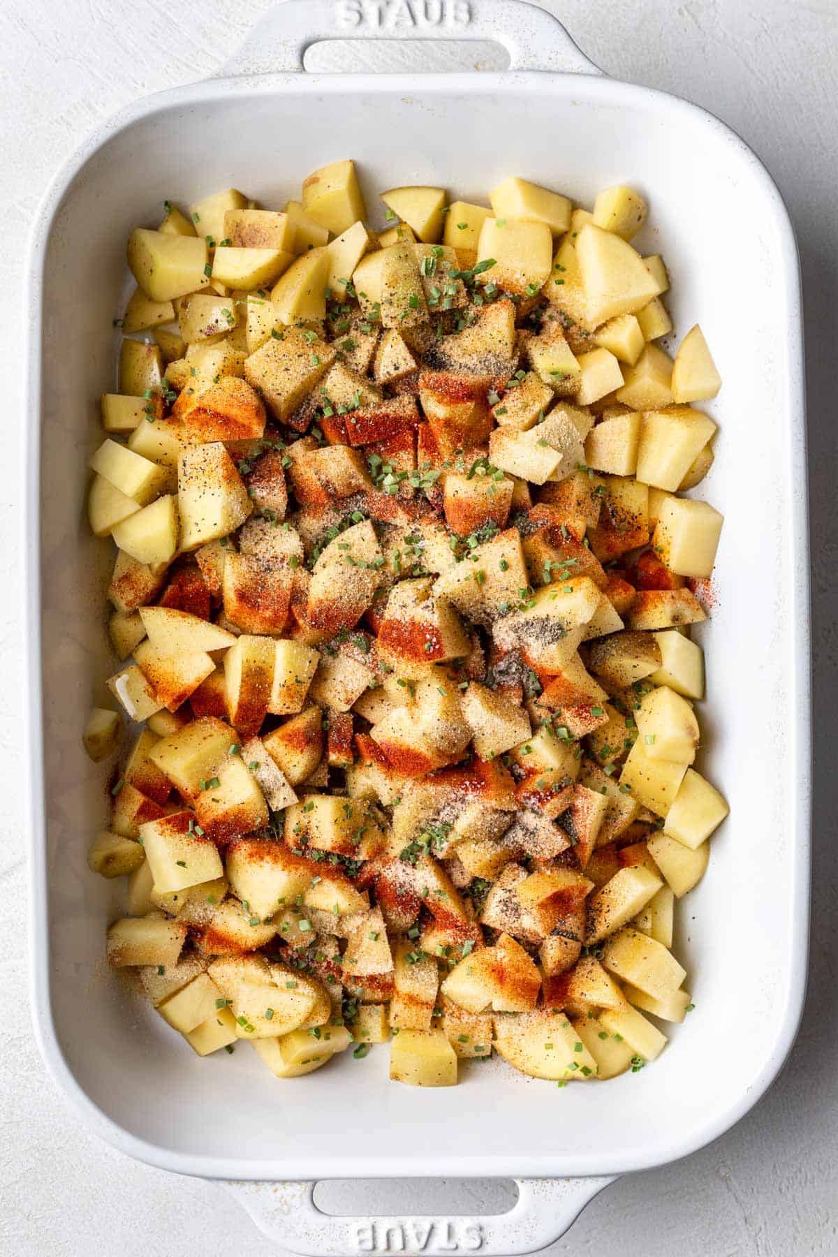 Uncooked potatoes with spices drizzled over top in baking dish.