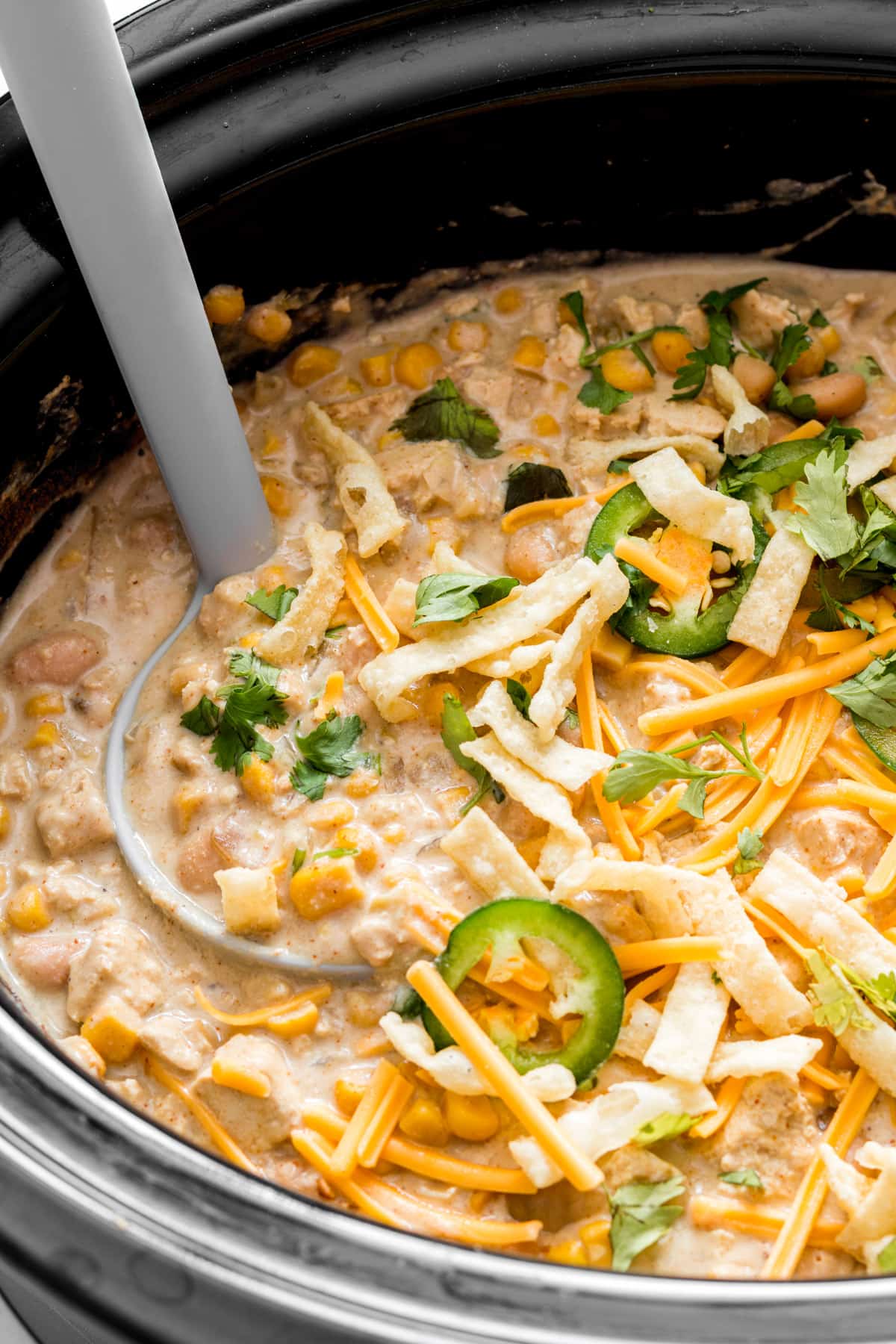 Ladle full of white chicken chili after cooking topped with garnishes.
