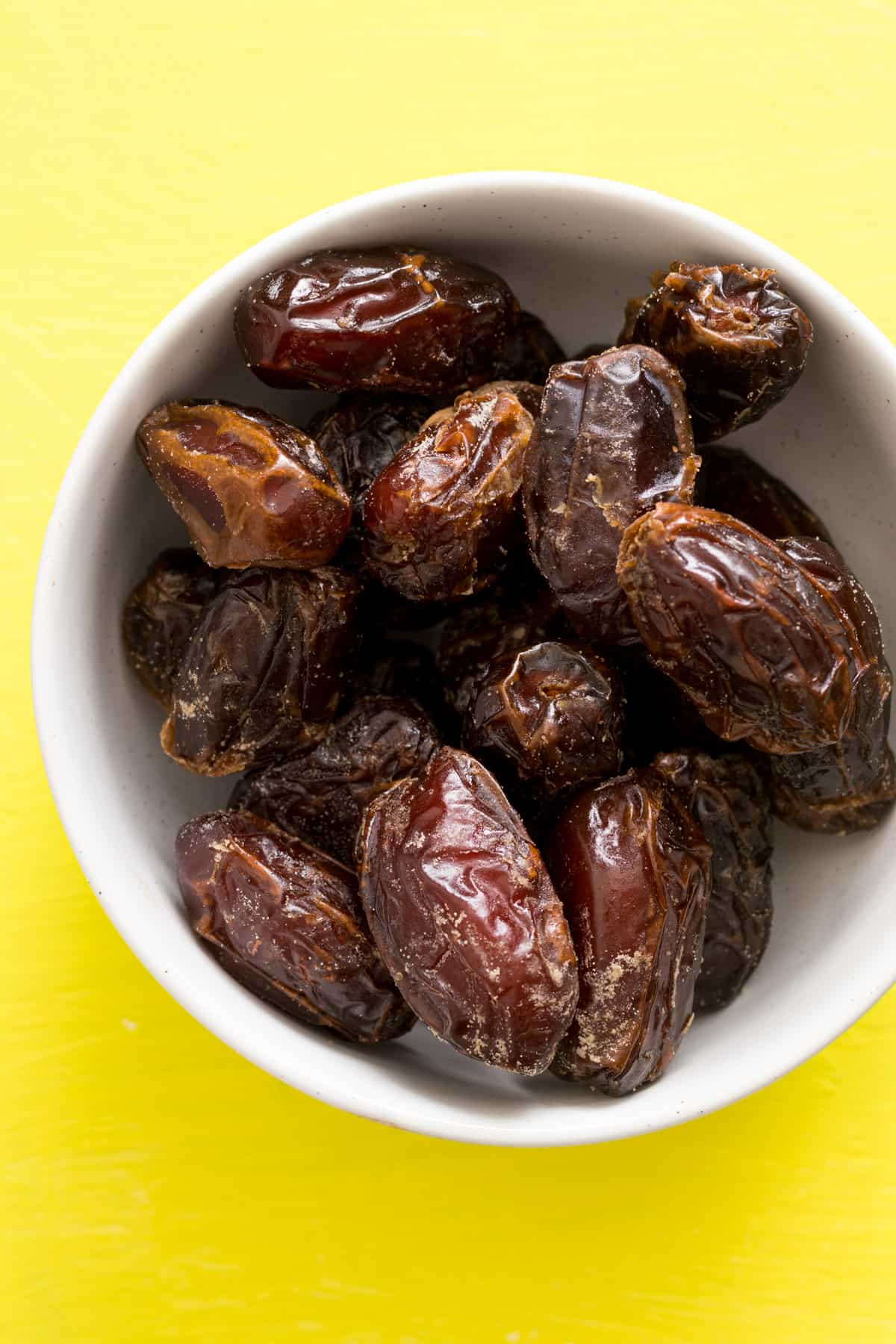 Dates in white bowl on green background.