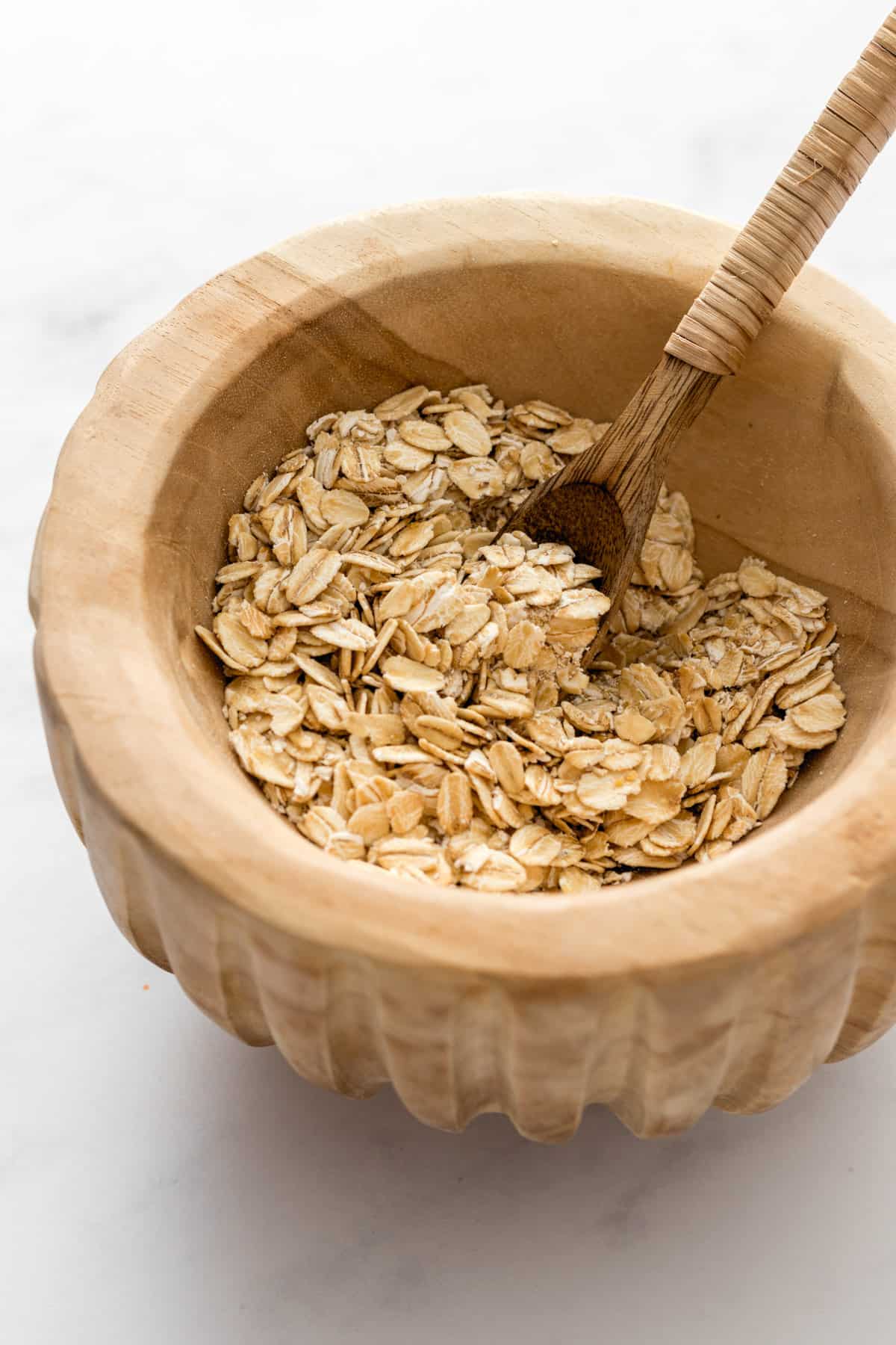 A wooden bowl and spoon with rolled oats.