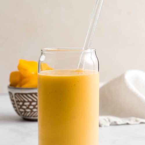 A yellow smoothie in glass cup with glass straw.