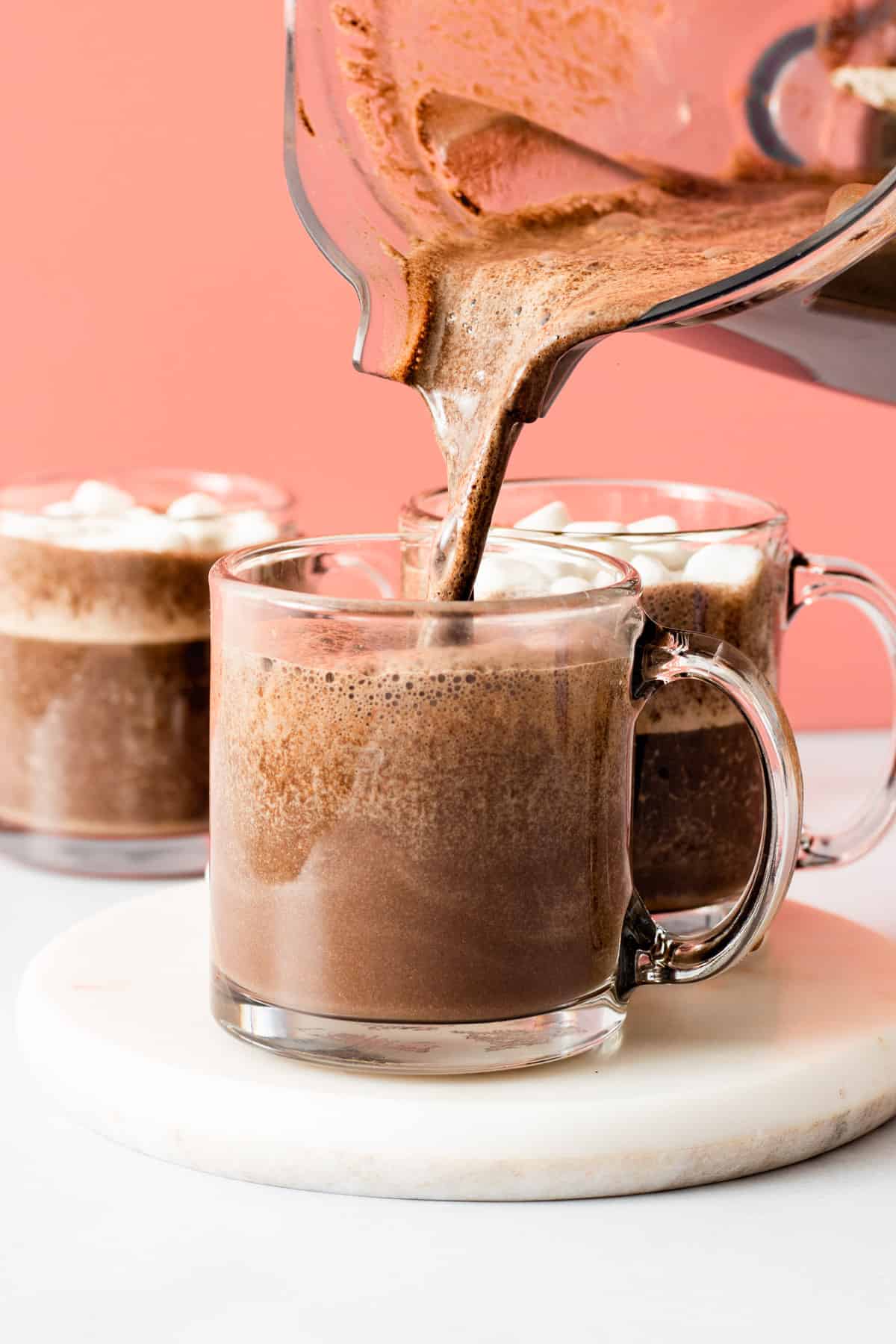 Pouring hot chocolate into clear glass mug.