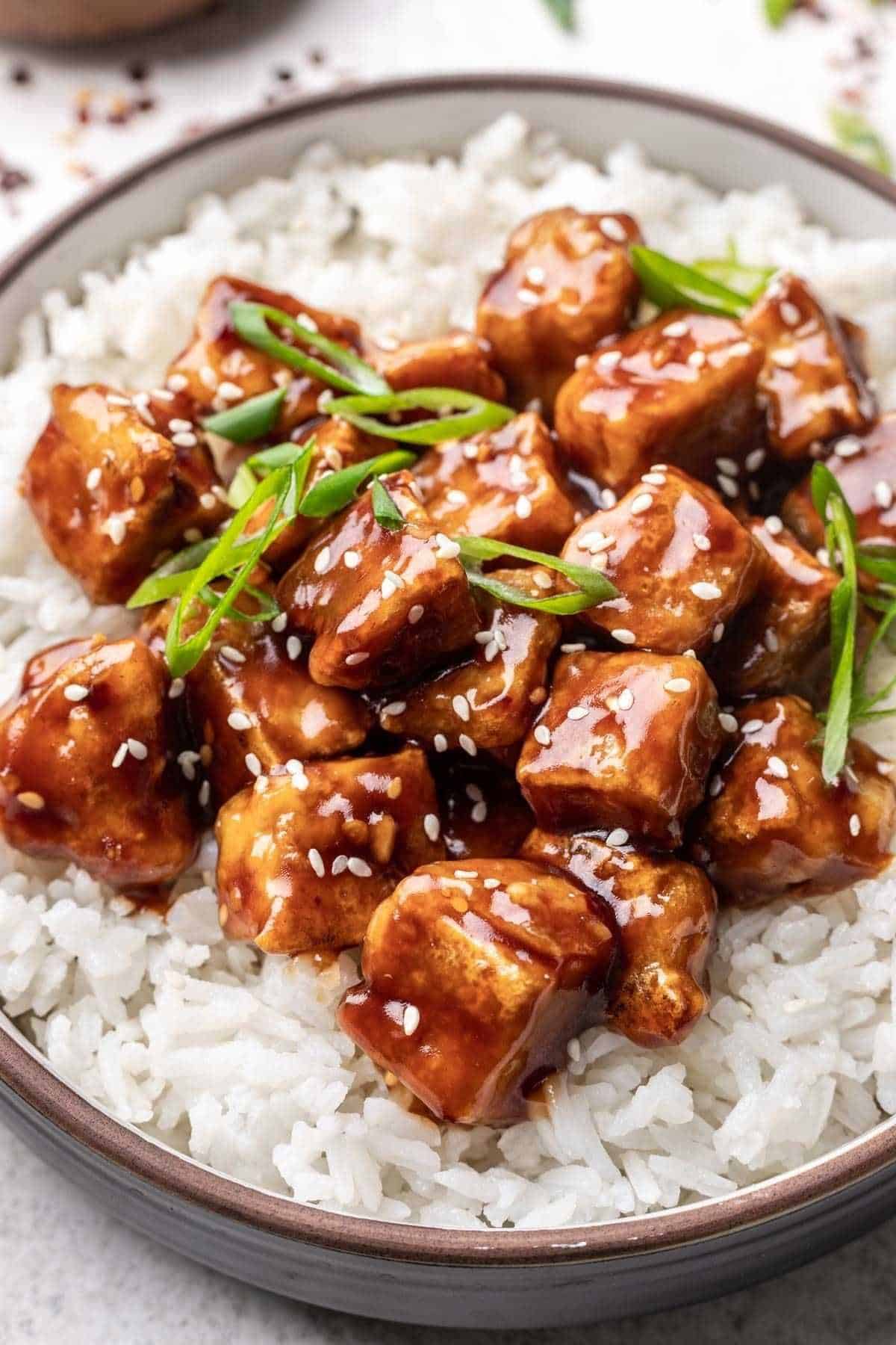 Close up of General Tso's tofu served over white rice and garnished with sesame seeds and green onion.