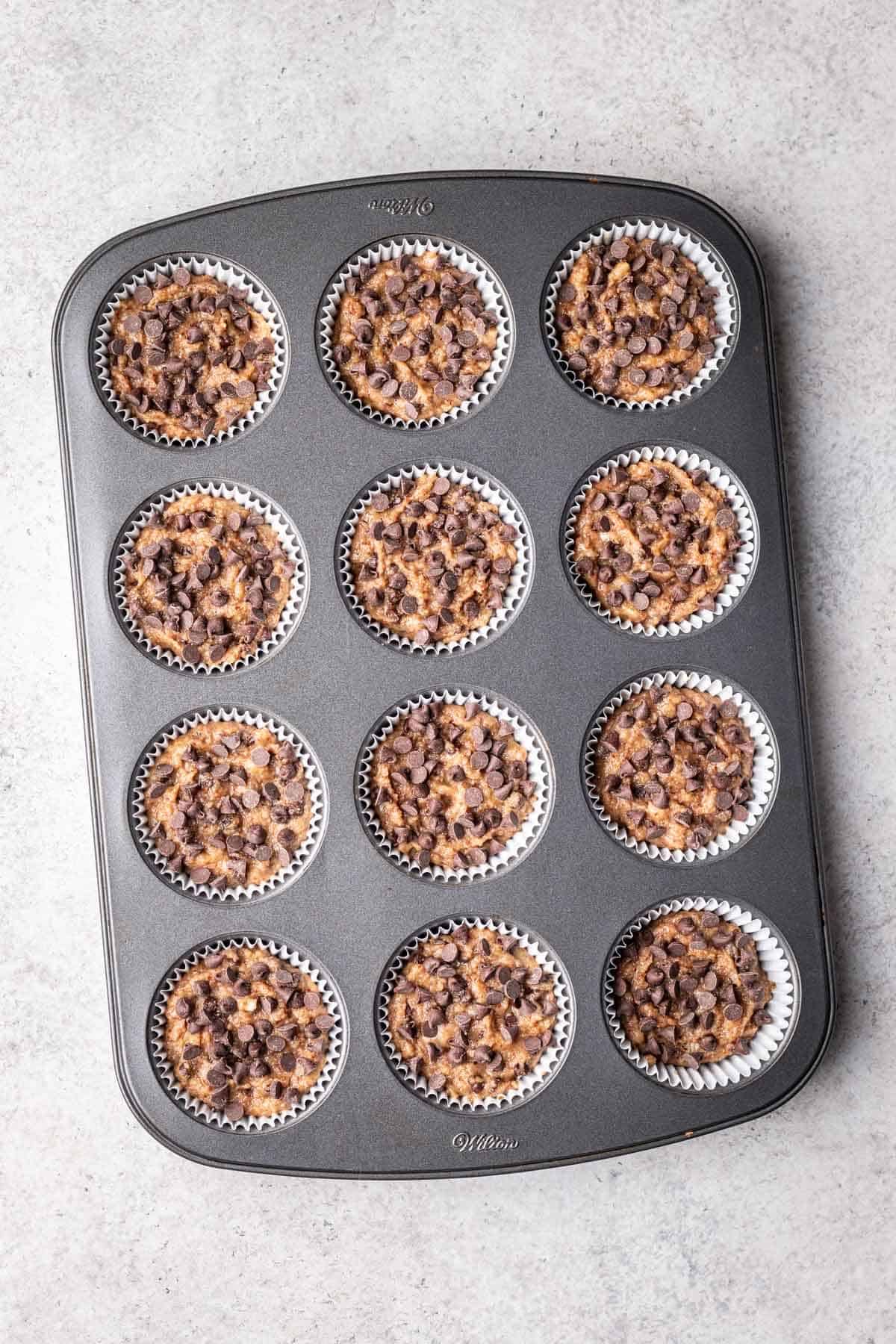Muffin batter topped with mini chocolate chips in muffin tin before baking.