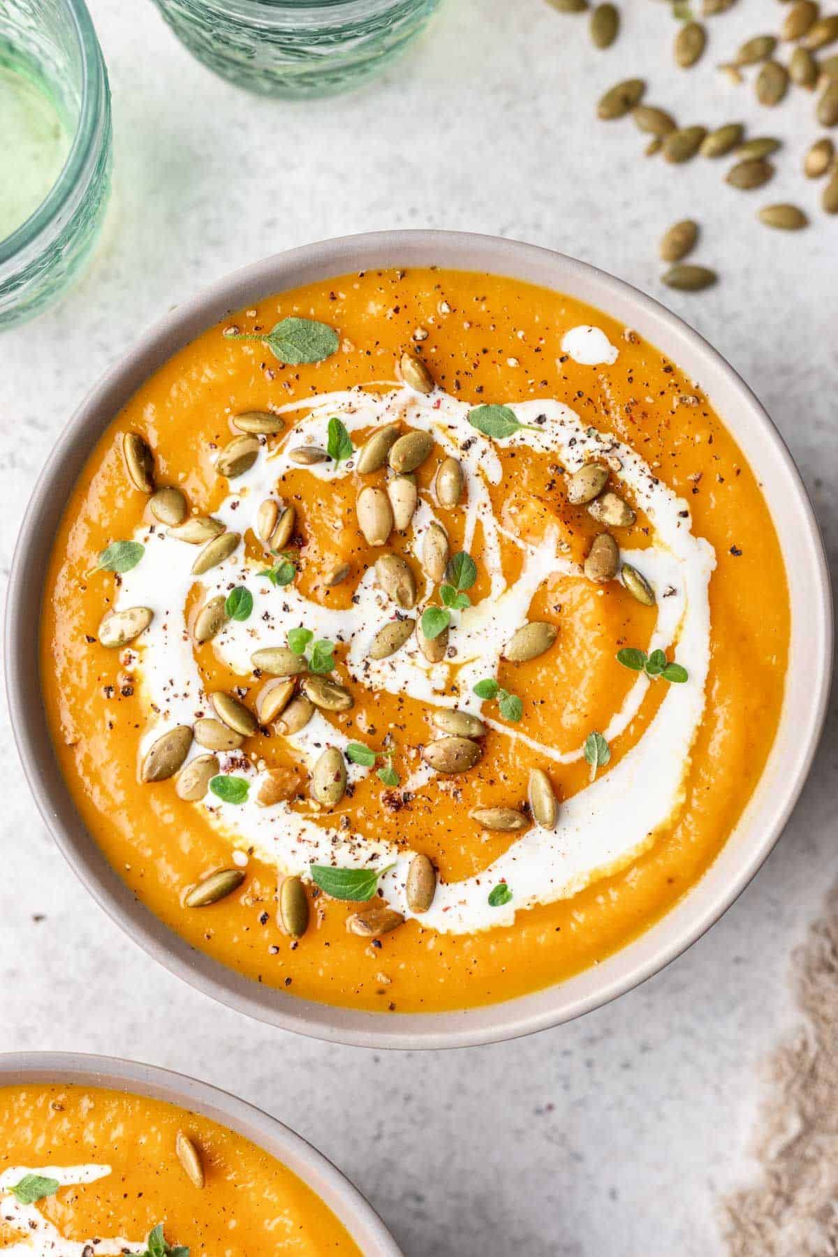 Butternut squash soup garnished with cream, pumpkin seeds, and herbs.