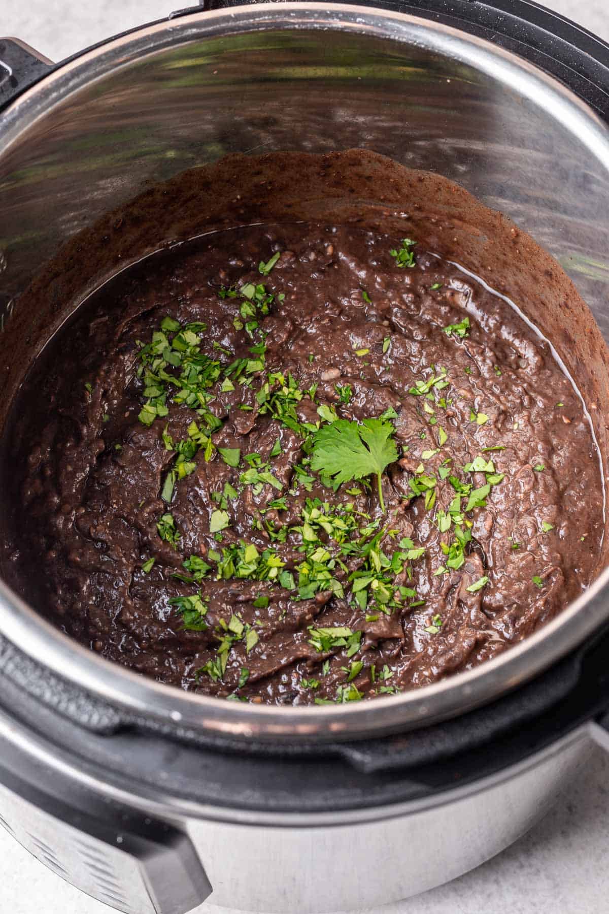Black refried beans in the Instant Pot garnished with fresh cilantro.