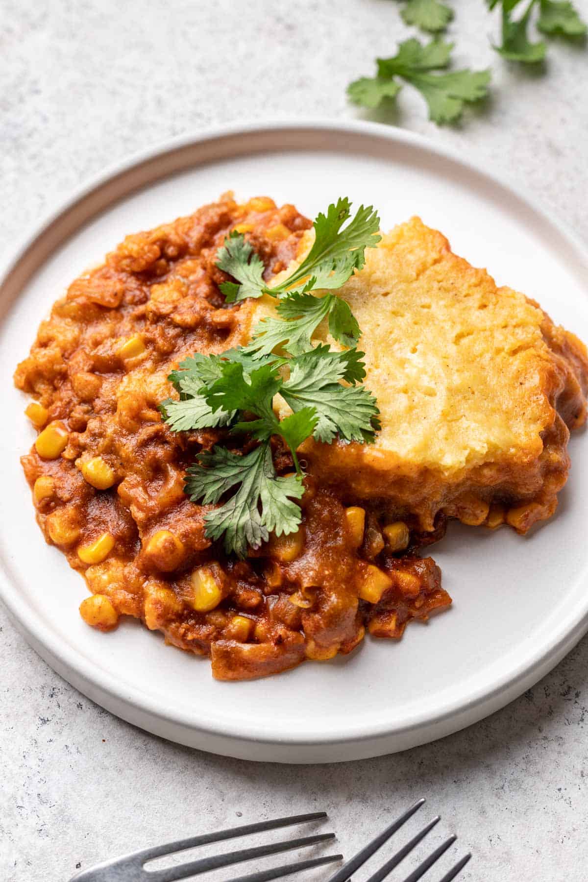 Vegan tamale pie with corn topping served on a plate with fresh cilantro.