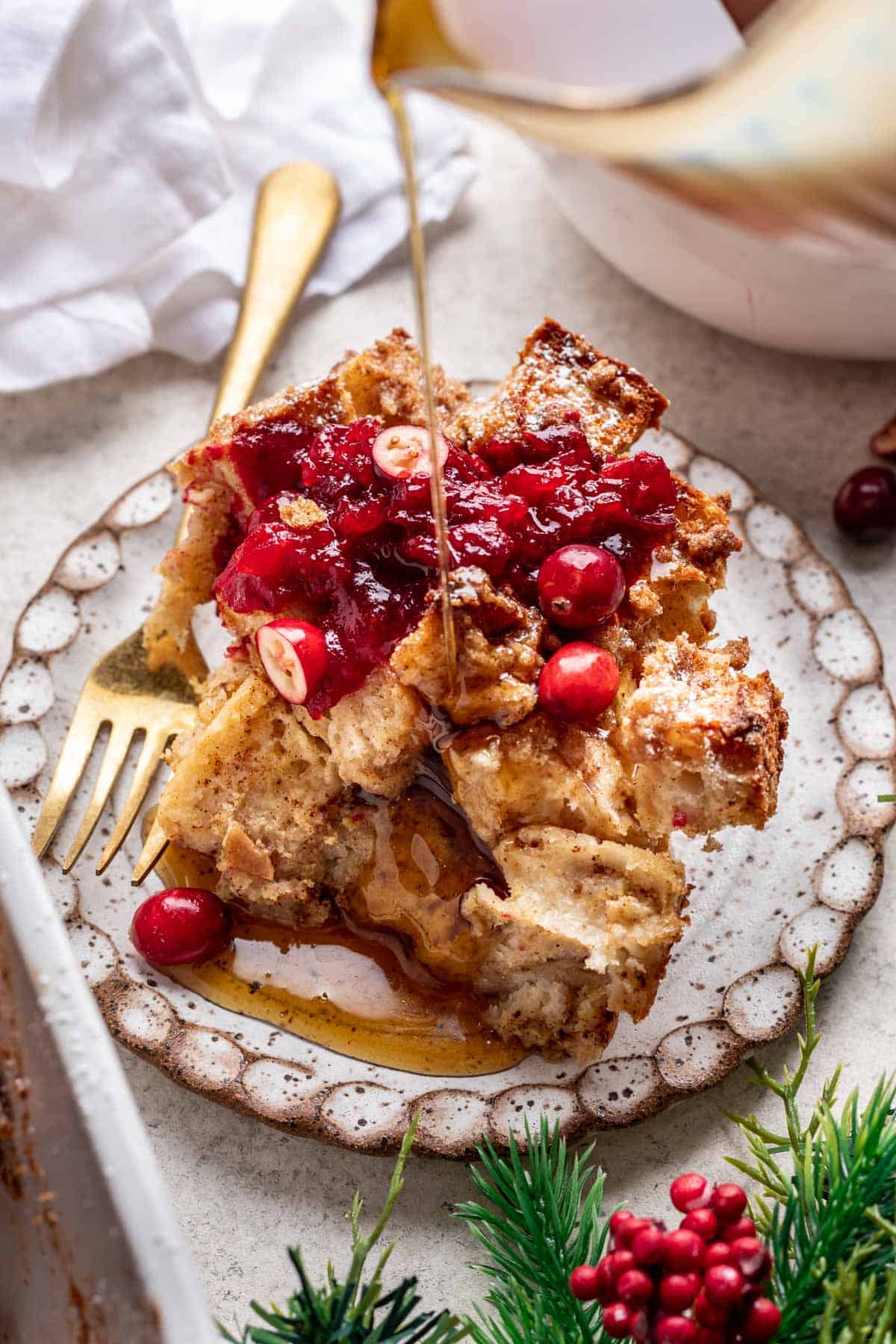 Serving of french toast casserole topped with cranberry sauce and maple syrup.