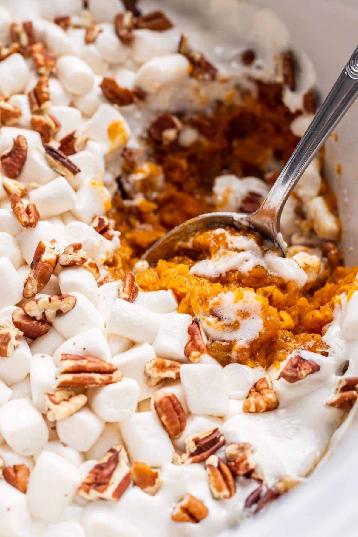 Sweet potato casserole topped with gooey marshmallows and chopped pecans in slow cooker bowl.
