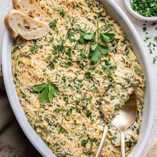 Final spinach artichoke dip garnished with fresh herbs and sliced bread for serving.