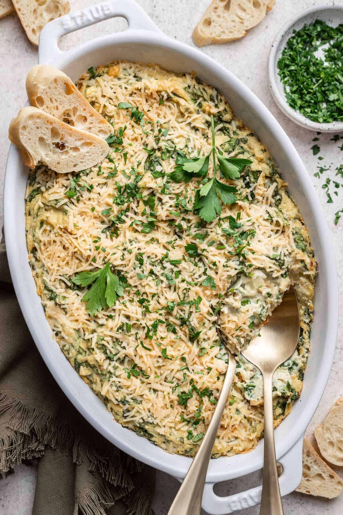 Final spinach artichoke dip garnished with fresh herbs and sliced bread for serving.