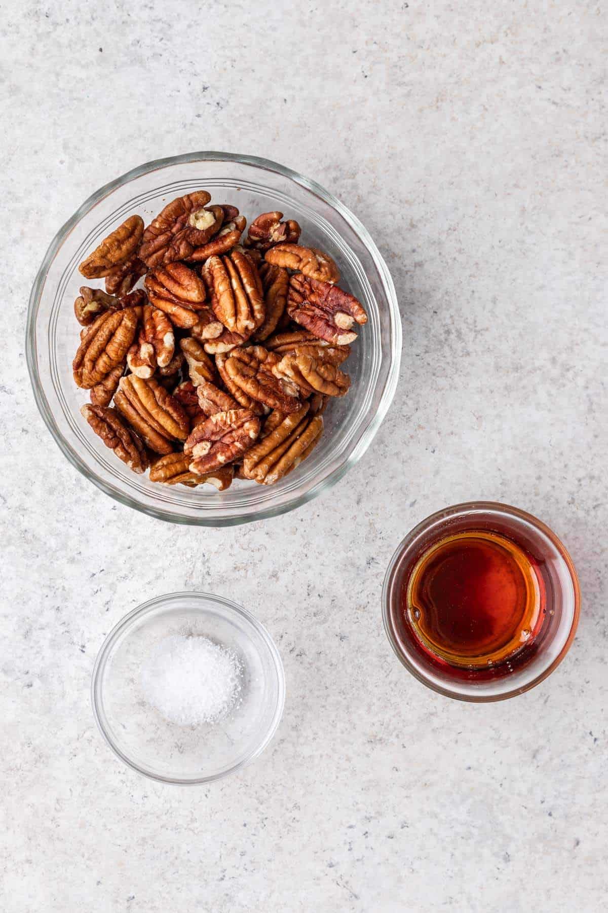 Pecans, maple syrup, and salt measured in individual glass bowls.