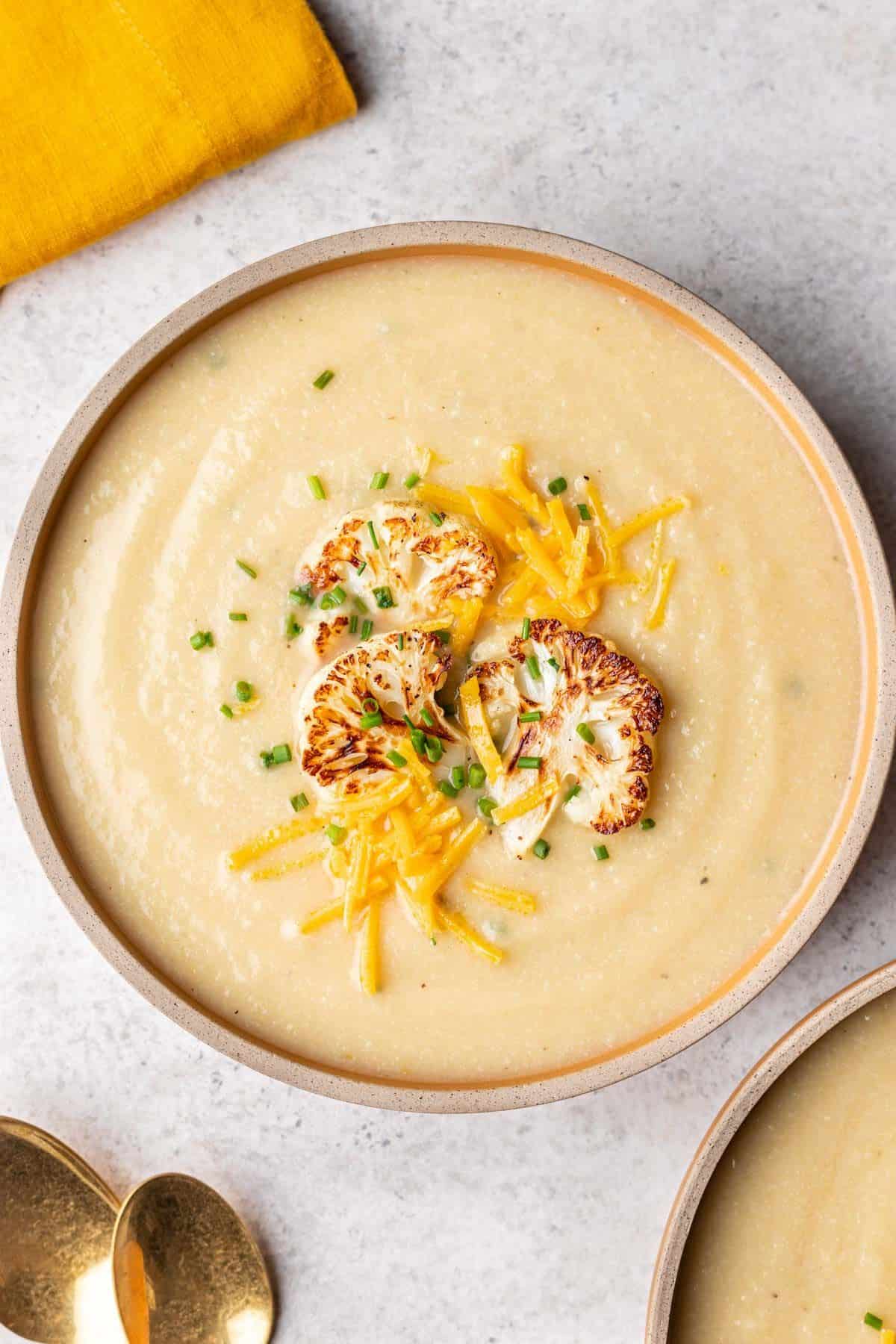 Serving bowl of cauliflower soup garnished with toppings. 