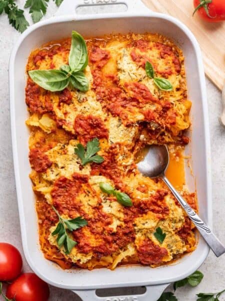 Spaghetti squash lasagna baked in white casserole dish and garnished with fresh basil.