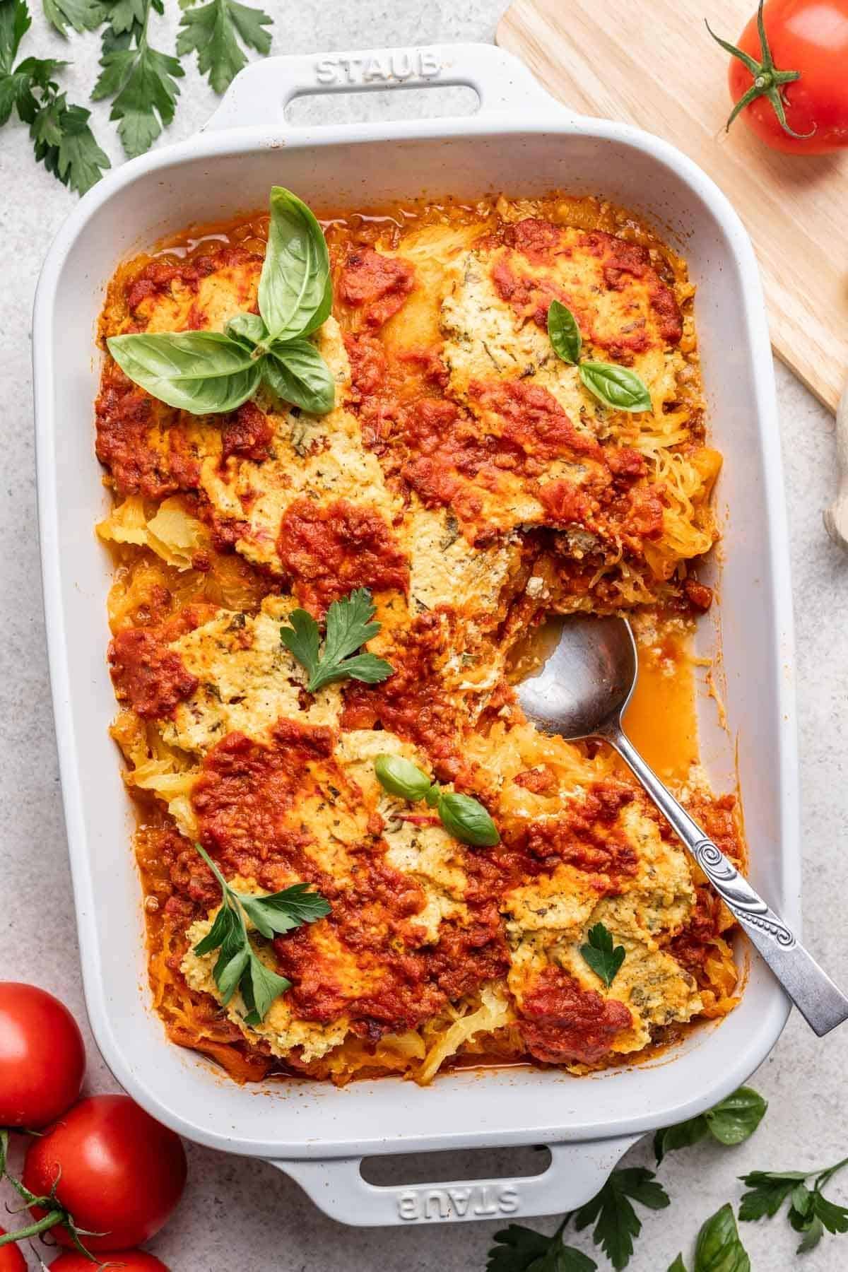 Spaghetti squash lasagna baked in white casserole dish and garnished with fresh basil.
