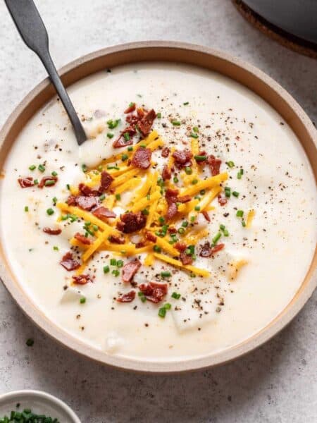 Bowl of vegan potato soup garnished with chives, cheddar cheese, and vegan bacon bits.