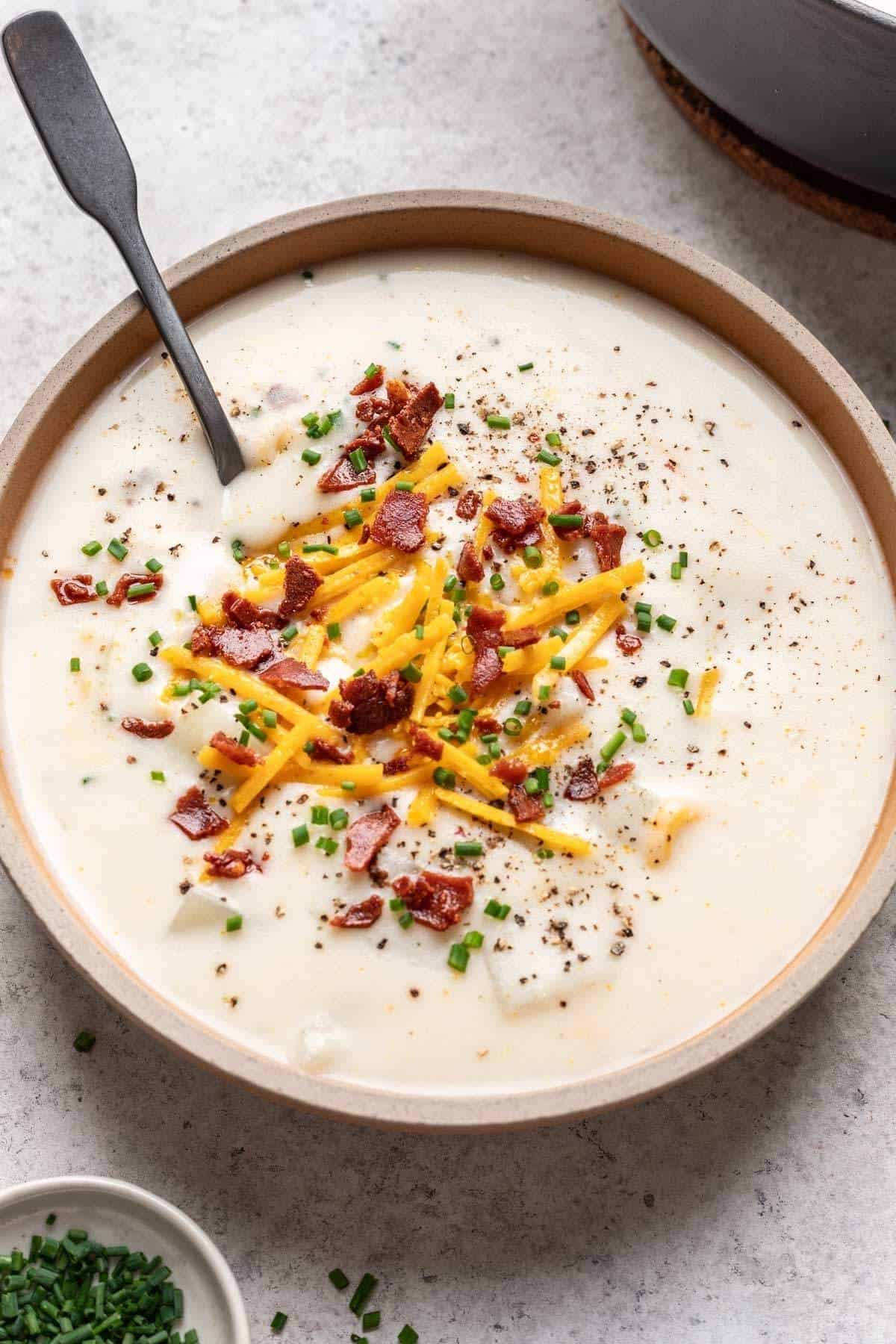 Bowl of vegan potato soup garnished with chives, cheddar cheese, and vegan bacon bits.