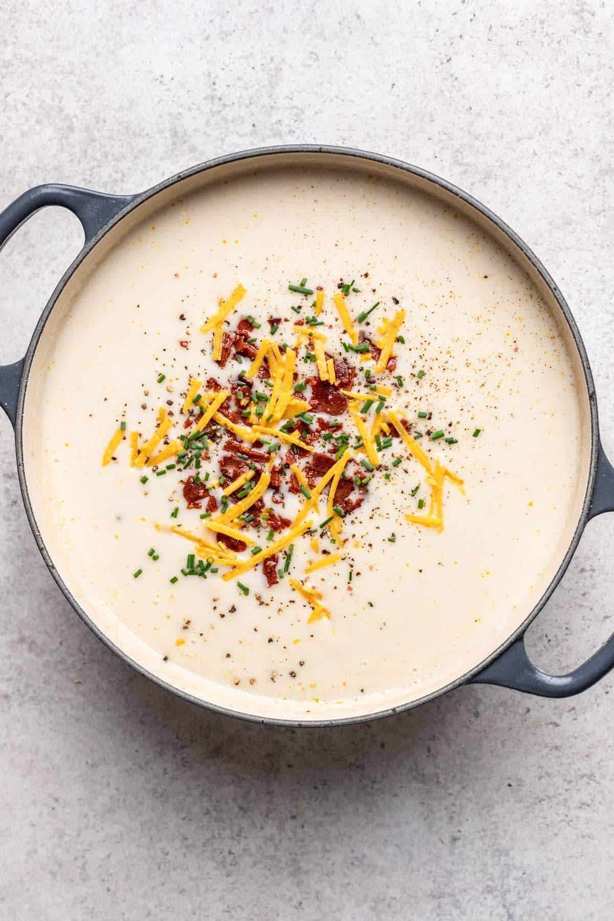 Final potato soup in large soup pot garnished with chives, vegan cheddar cheese, and vegan bacon bits.