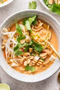 Serving bowl of red curry ramen garnished with crushed peanuts, fresh cilantro, and bean sprouts.