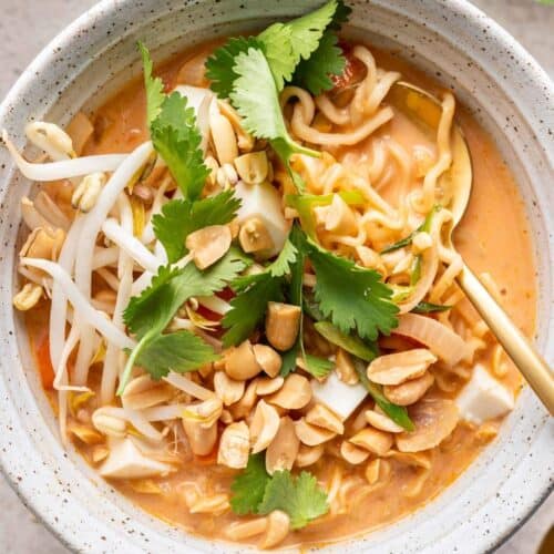 Serving bowl of red curry ramen garnished with crushed peanuts, fresh cilantro, and bean sprouts.