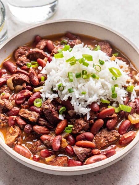 Bowl of Instant Pot red beans served with fluffy white rice, green onion, and freshly cracked black pepper.