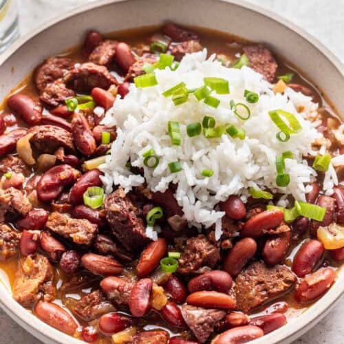 Bowl of Instant Pot red beans served with fluffy white rice, green onion, and freshly cracked black pepper.