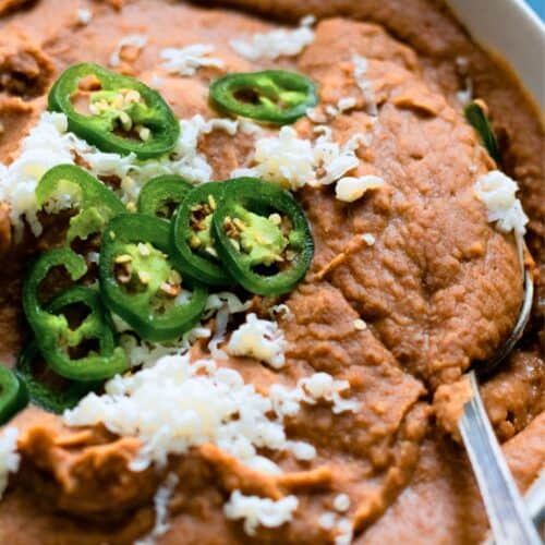 Bowl of refried beans topped with sliced jalapeño and cheese.