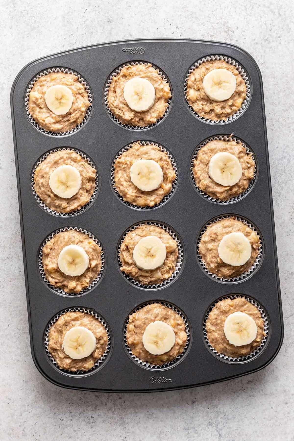 Unbaked muffins in muffin tin topped with a thin slice of banana.