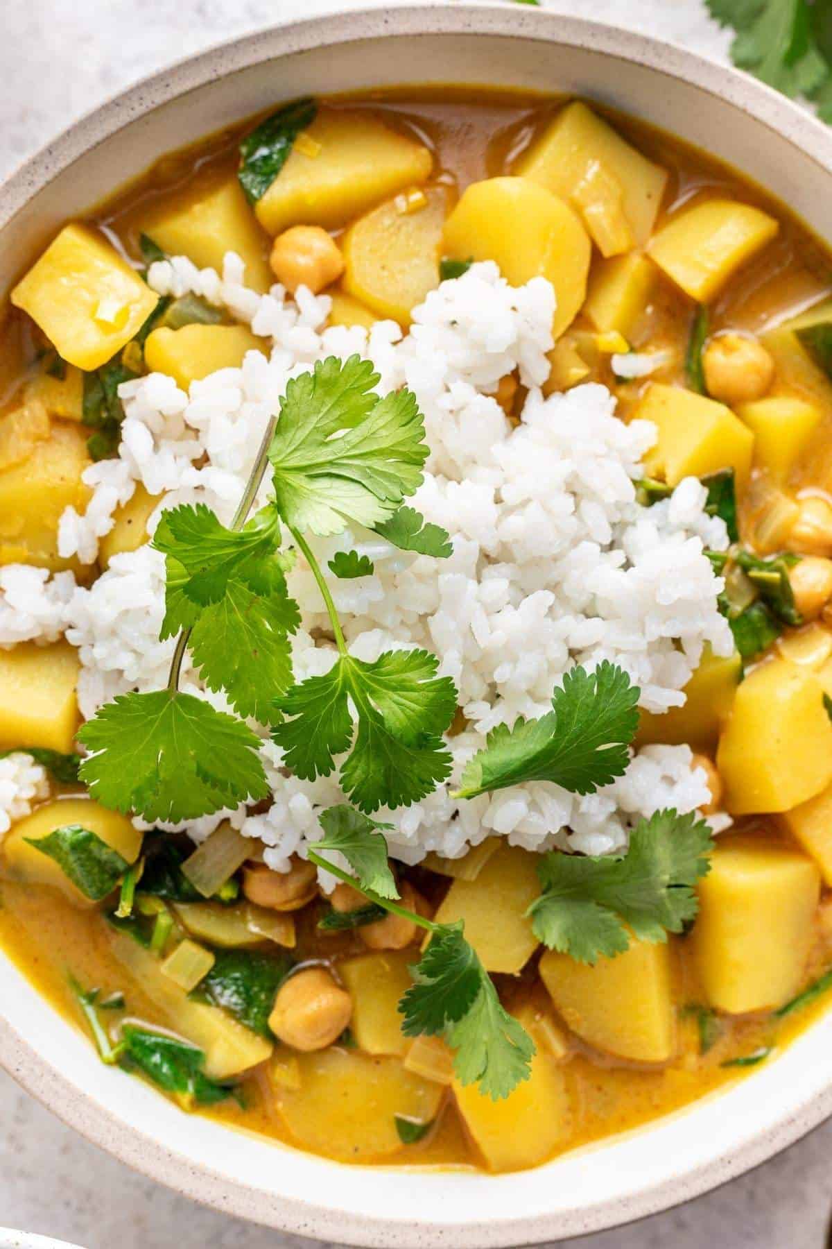 Closeup of yellow curry with potatoes, chickpeas, and white rice.