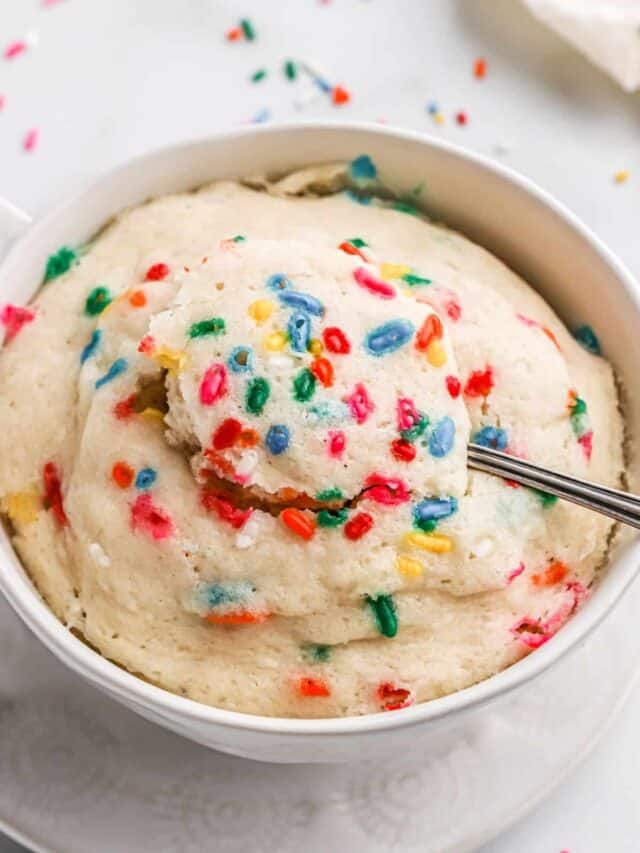 Vanilla mug cake microwaved with funfetti sprinkles in white mug with spoon.