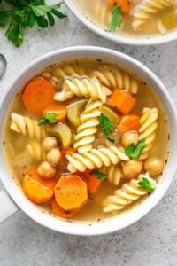 Chickpea noodle soup in white mug bowl.